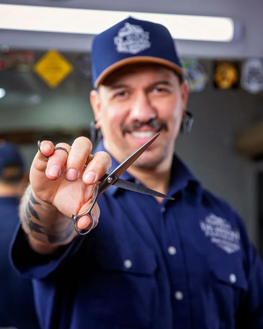 Lächelnder Barbier hält eine Schere in die Kamera – Website erstellen lassen für Barbershops und Friseure